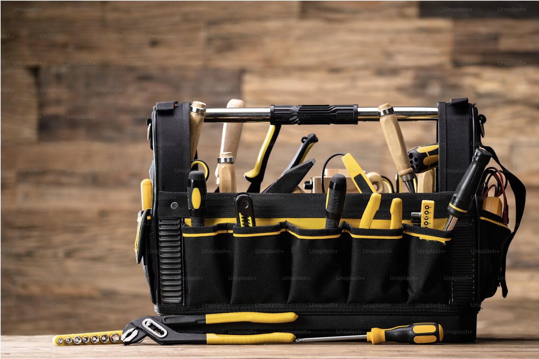 A black and yellow toolbox loaded with hand tools on a wooden surface